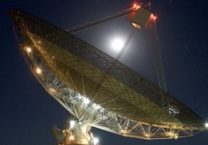 An almost full moon shines brightly above he CSIRO Parkes Radiotelescope.
